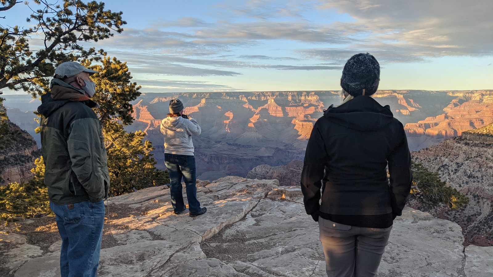 Three people stand on an outcropping of rock looking out over Grand Canyon