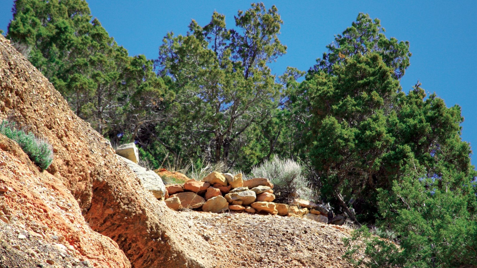 A pile of reddish colored rocks sit on the crest of a small hill in the desert.
