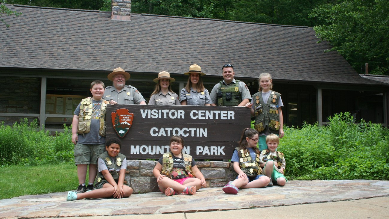A group of park rangers and children posing around a visitor center sign.