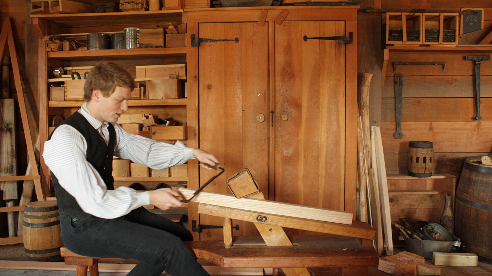 A man in 1840s clothing works on a carpentry project.