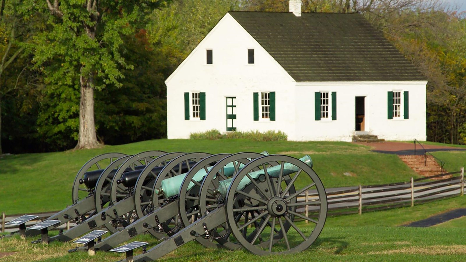 Four cannons stand on a green lawn, a white church building is in the background.