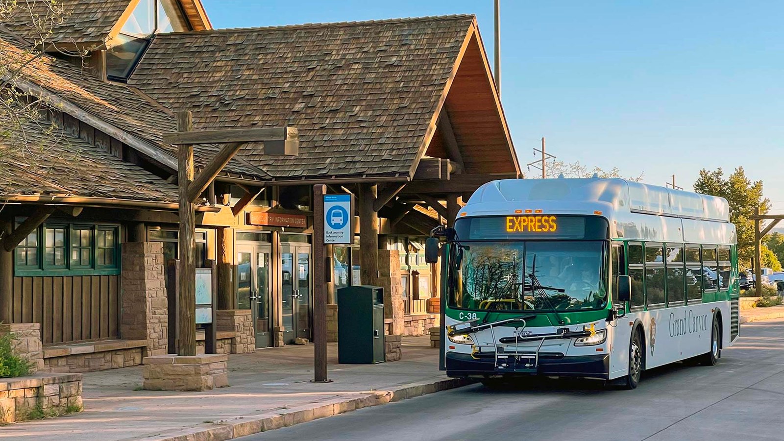 a white and green bus is parked in front of a rustic building with gabled shake roofs.