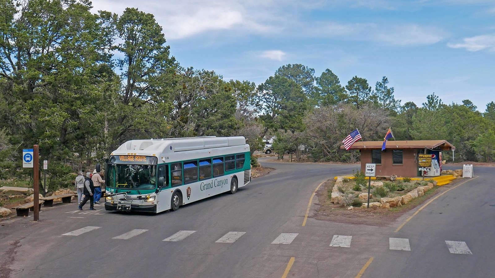 A white and blue bus waiting at a but stop with several benches and a route sign.