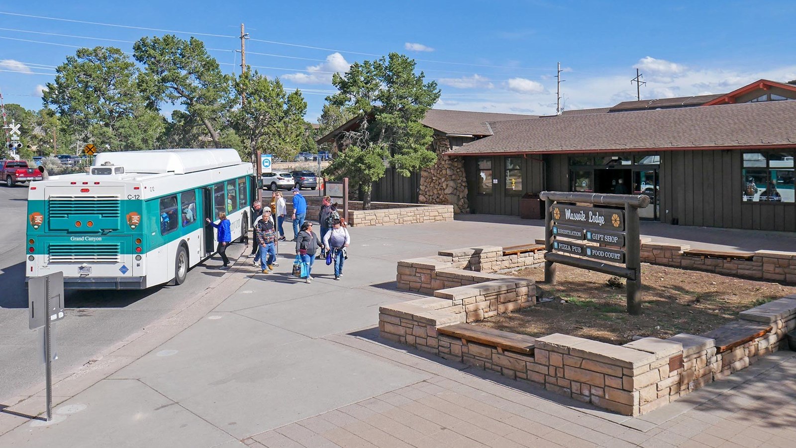 a white and green bus at an outdoor stop in front of a brown lodge building. People are boarding.. 