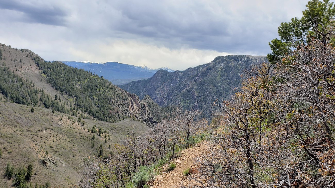 A trail leading around a cliff edge with a view of mountains