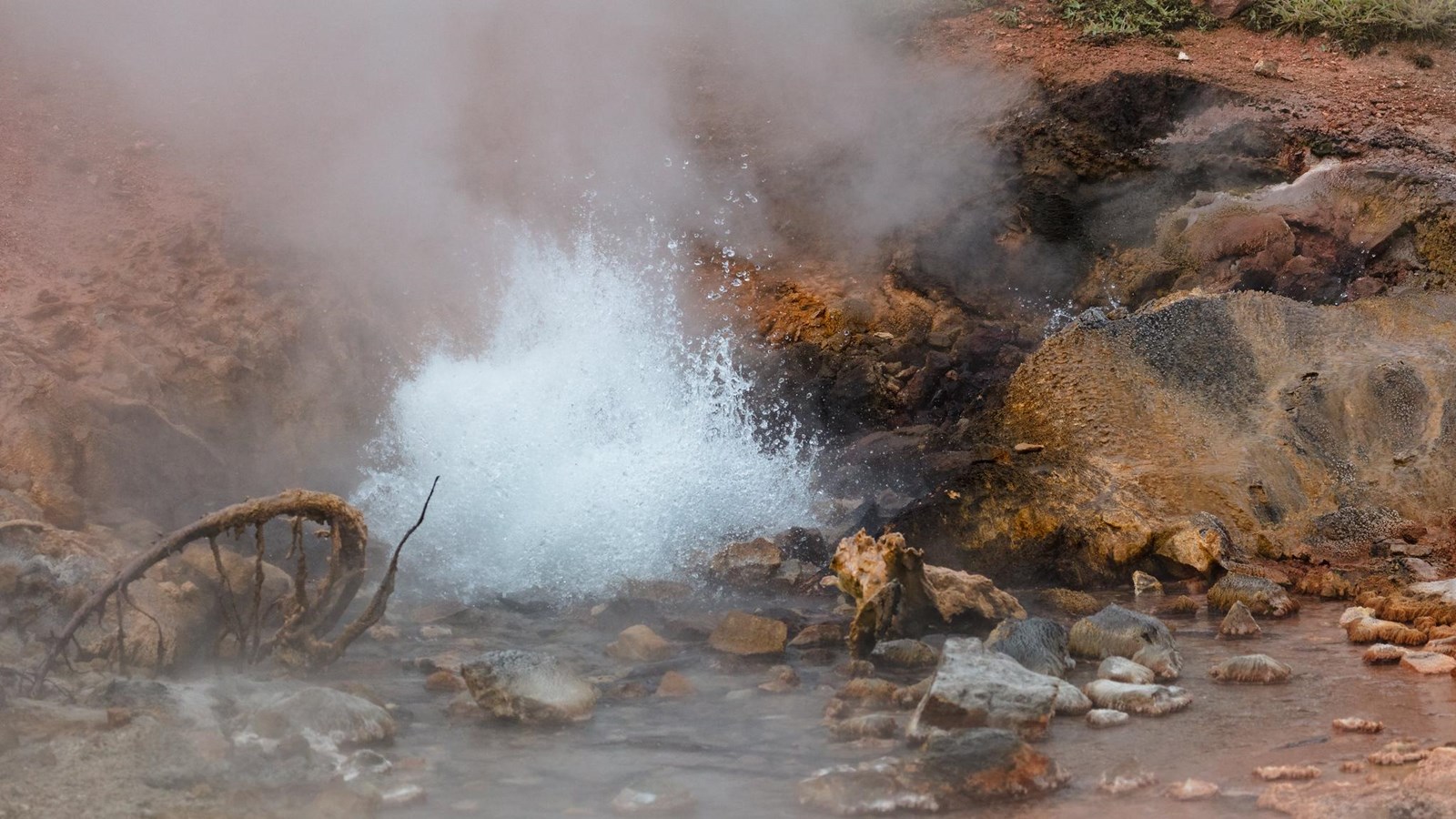 Water erupts out of a pool of rust colored water surrounded by rust-colored mineral deposits