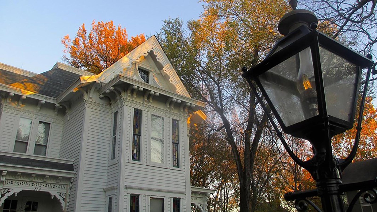 Historic street lantern with a large white wooden historic house in the background.