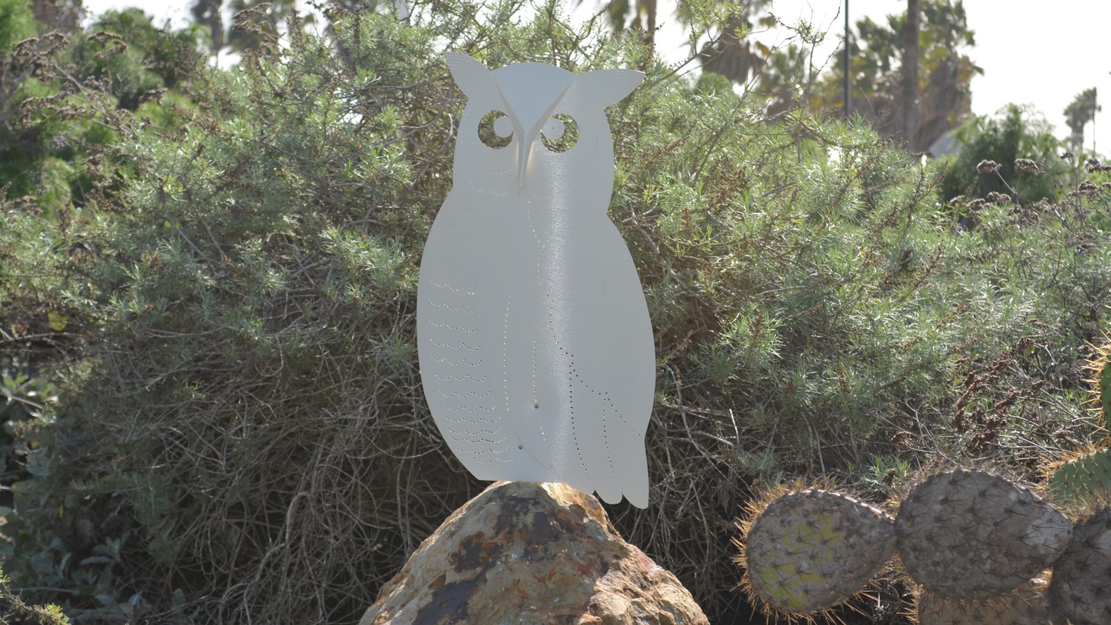 A two-foot-tall long eared owl sits atop a large pointed rock. Hole punch line designs outline the b