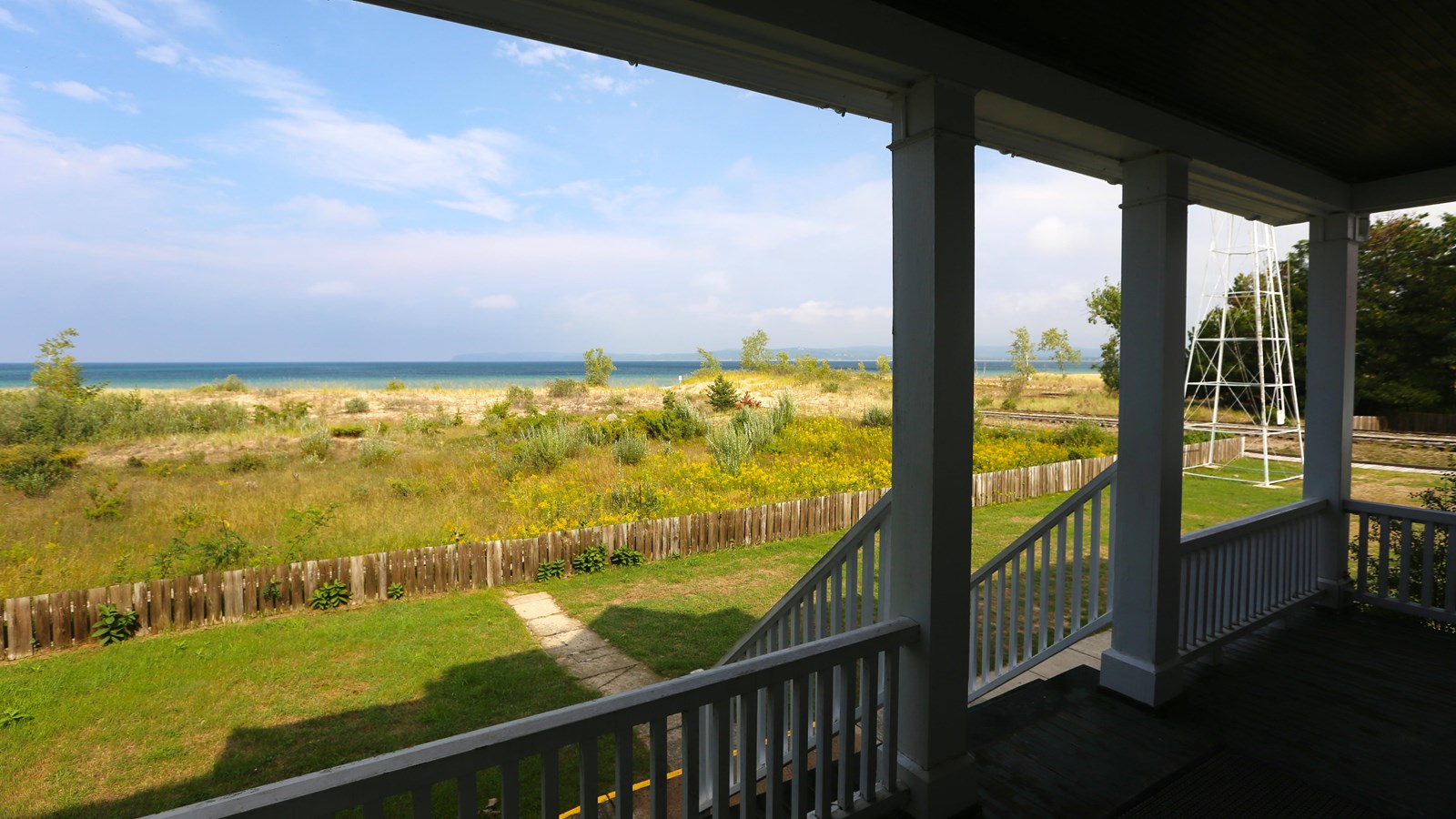 Looking from covered porch toward vegetated dunes, a strip of beach, and deep blue lake