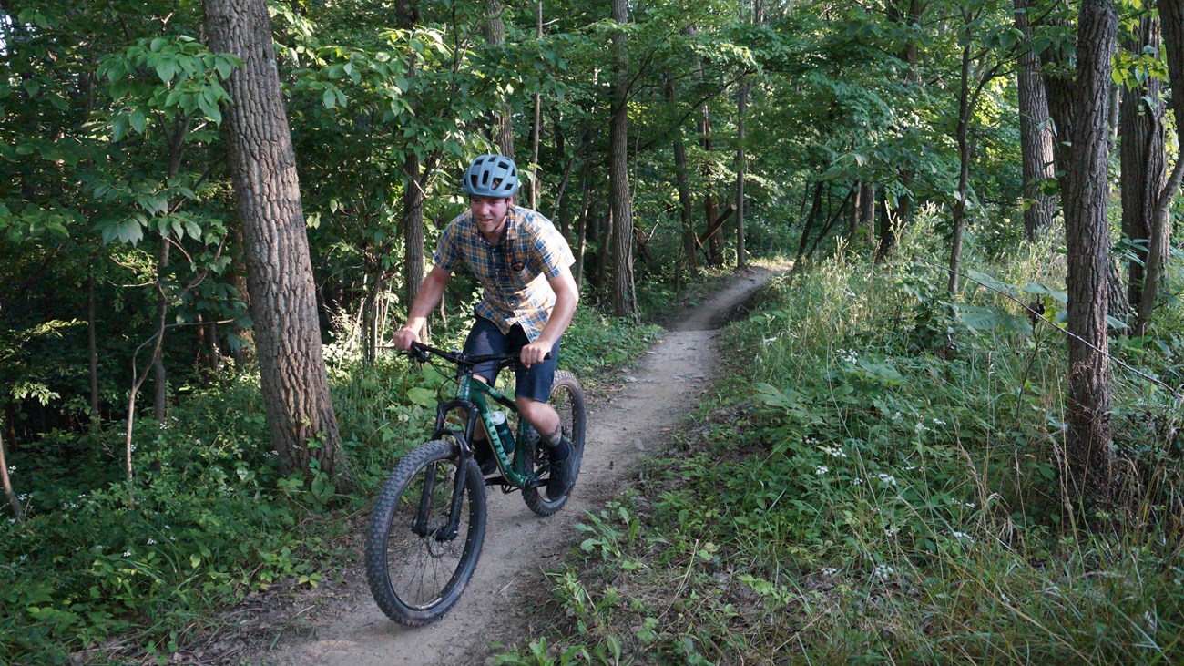 A person wearing a helmet cycles up a mountain bike trail. 
