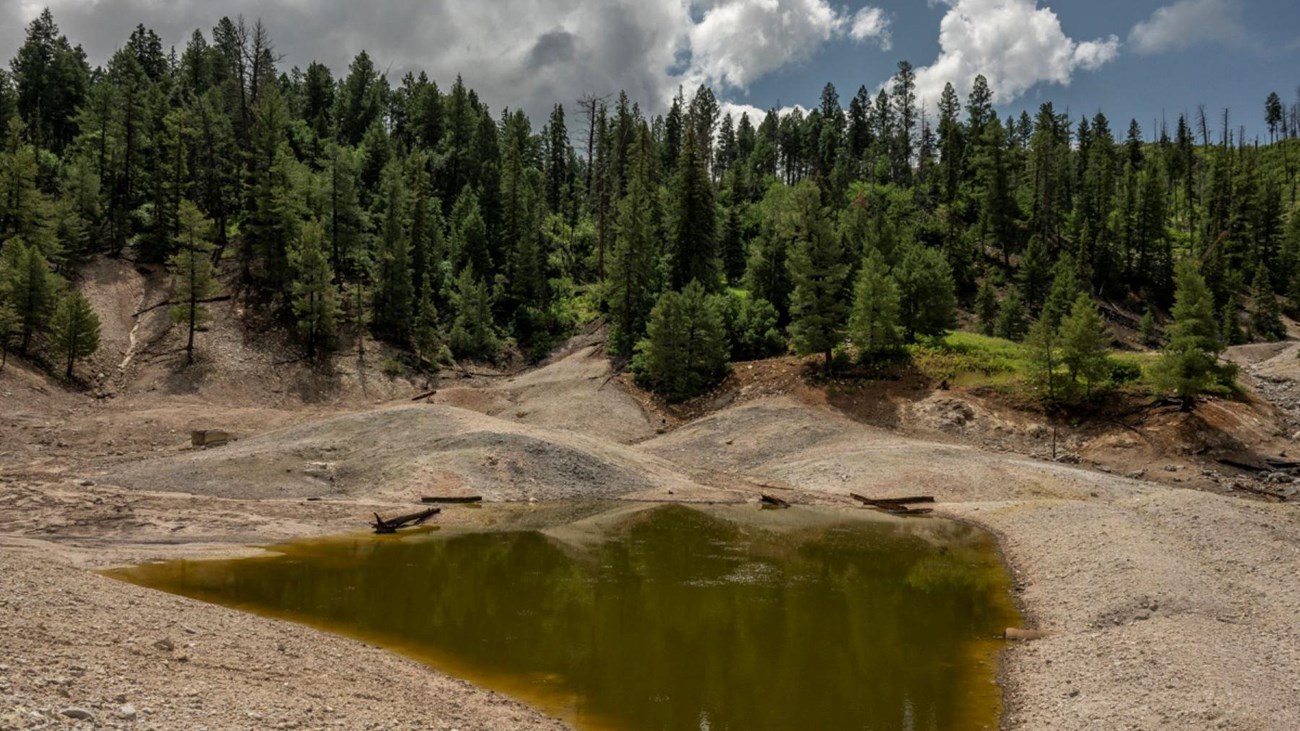 A green pond in a geothermal landscape of bleached gravel.
