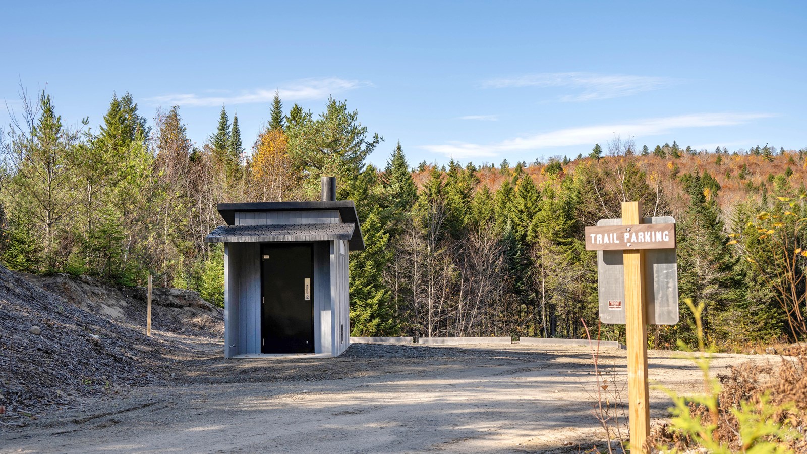A one-way dirt parking area with a vault toilet to the left of the entrance.