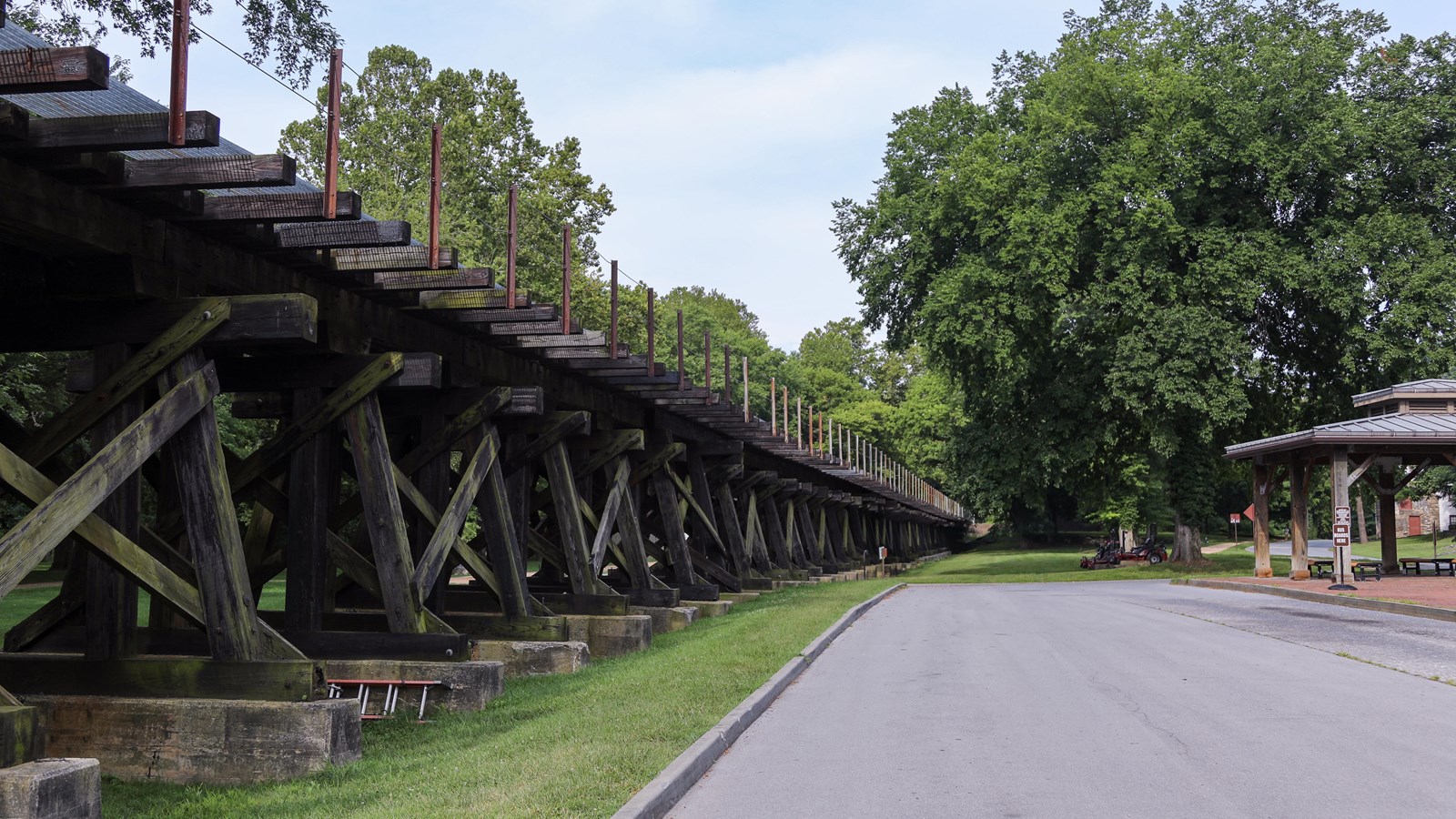 An elevated train track on wooden beams runs parallel to a roadway.