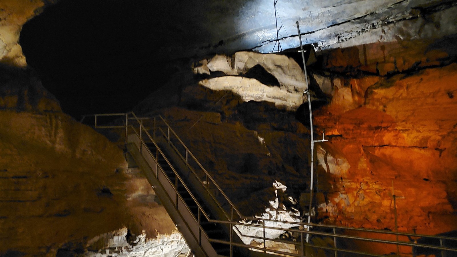 A metal staircase leads to a upper cave passage.
