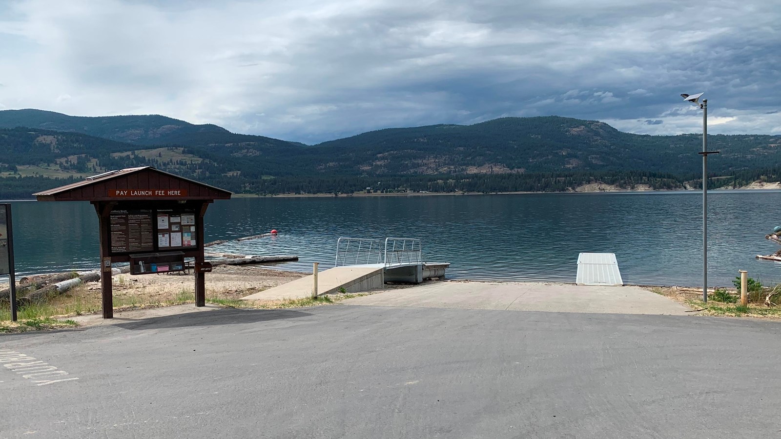 A brown kiosk next to a paved boat launch that extends into dark blue water.