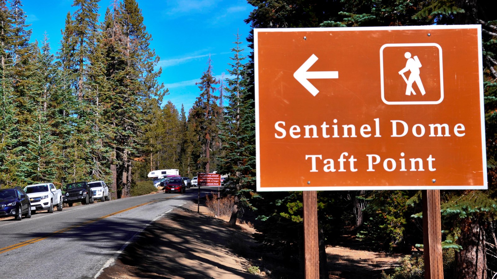 Brown metal trailhead sign with arrow alongside road