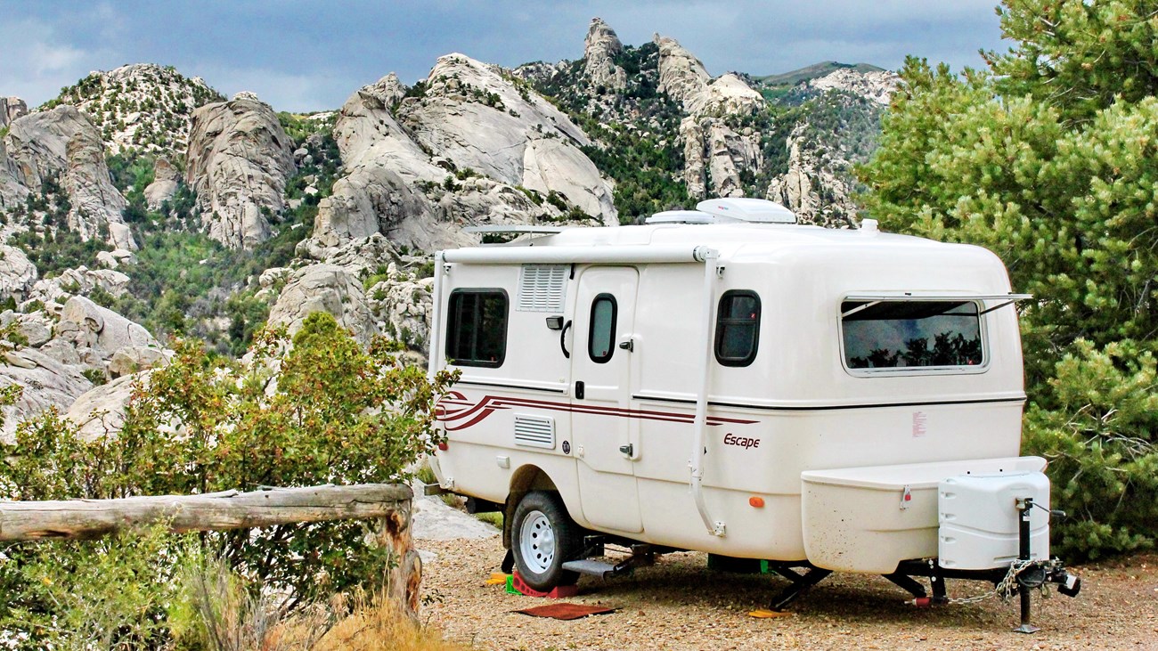 A small bumper pull camper parked with a spectacular view of distant granite formations.