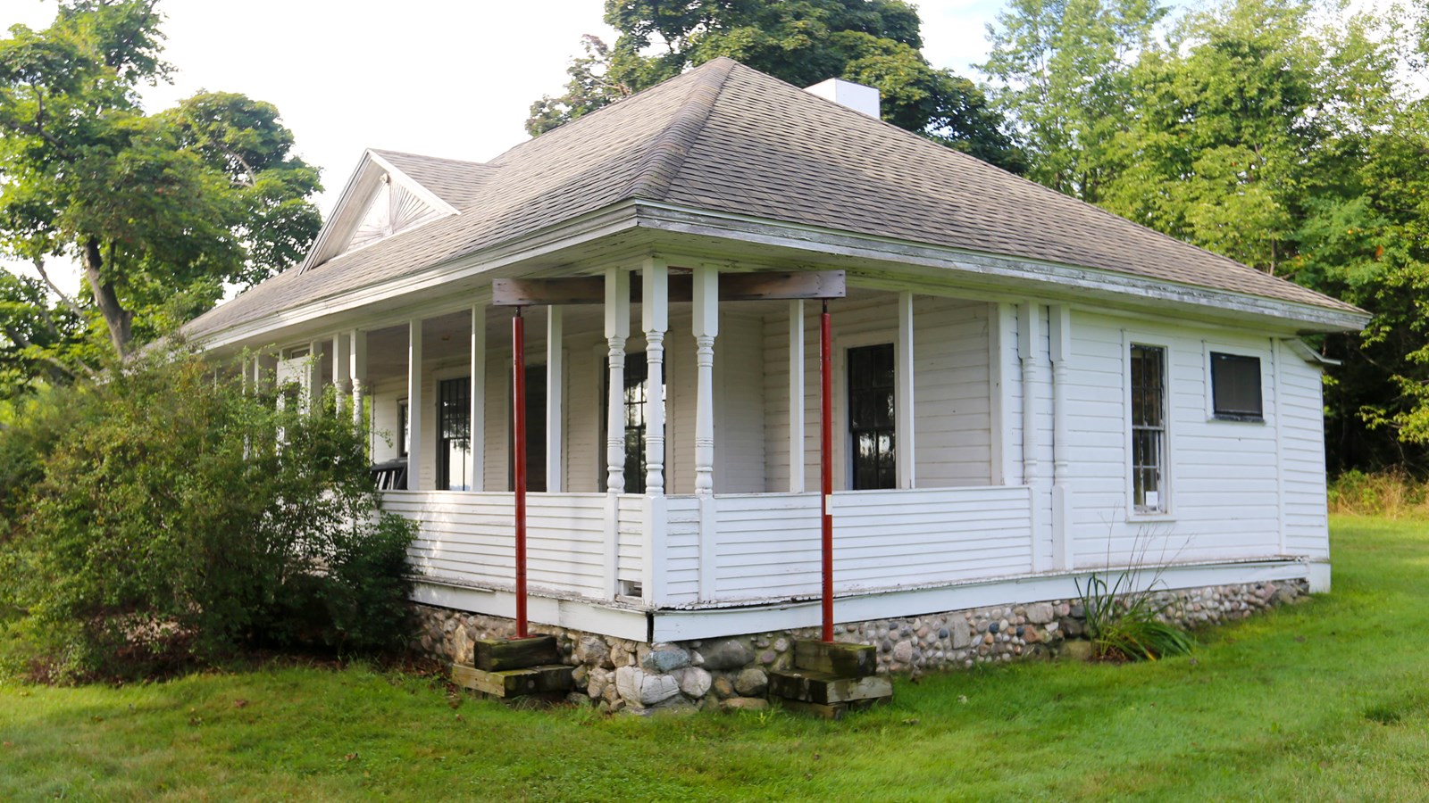 Corner of small, white cottage with three newell post supporting the covered front porch