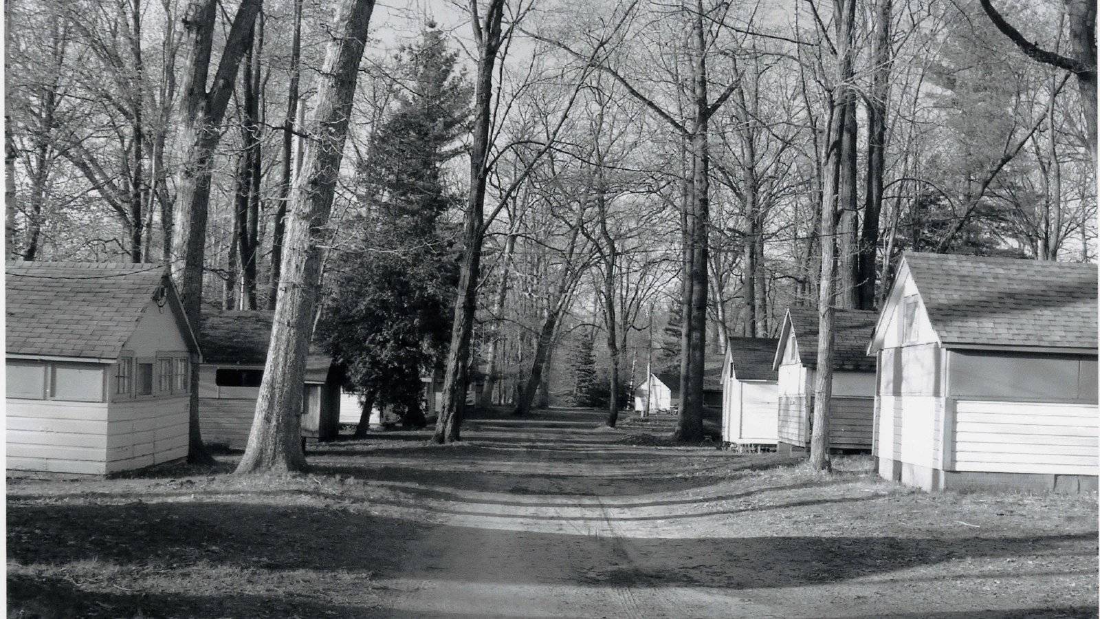 Dirt road lined by one-story white, slant-roofed buildings