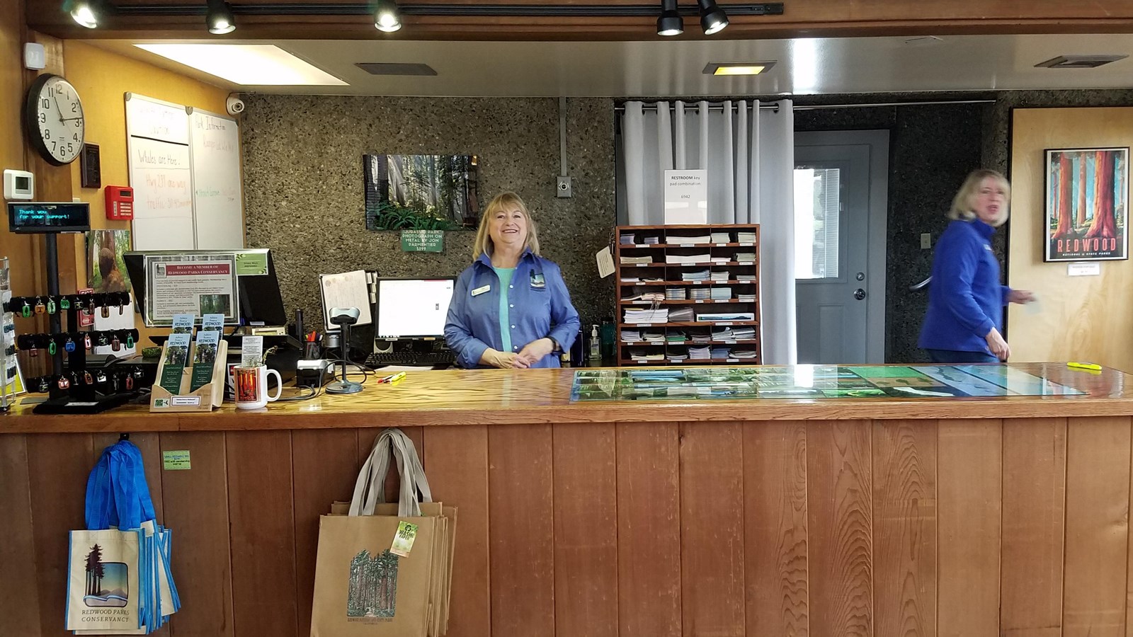 Two women in blue uniforms behind a sales desk.