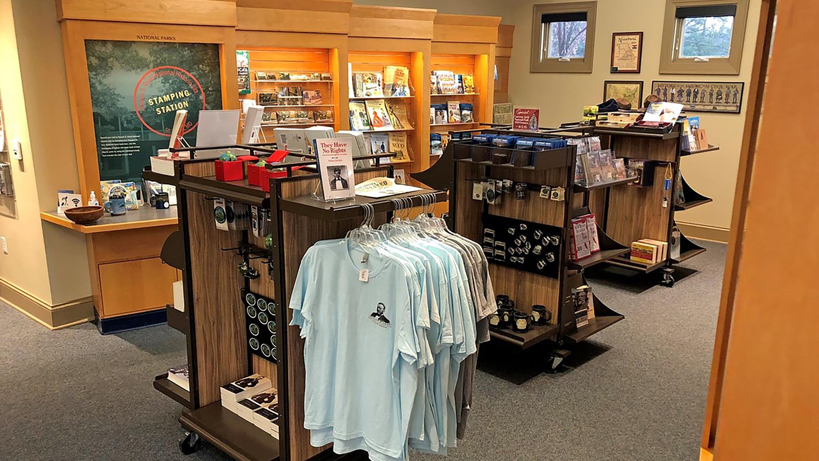 Tan wooden shelves containing books, ornaments, pins and t-shirts.
