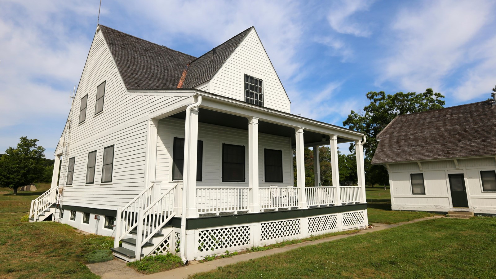 A two-story white clapboard structure with black-shingled gables and elevated front porch