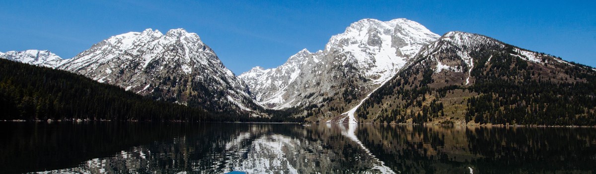 Snowy mountains are reflected on a glassy lake.
