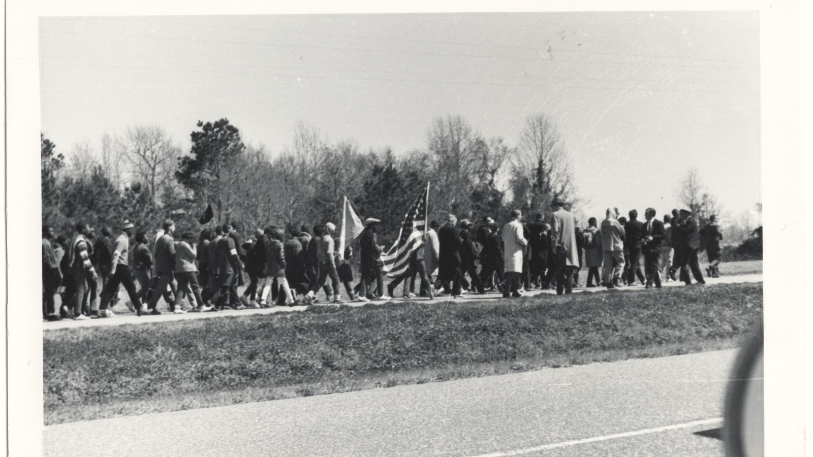 Scan of a black and white polaroid photo of a crowd of people walking on a rural highway.