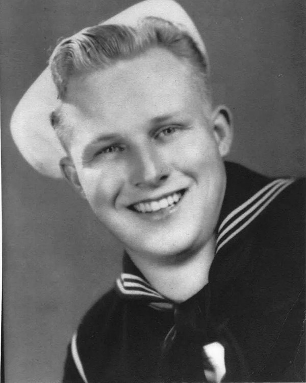 Black and white portrait of a sailor wearing a dark naval uniform and white cap on his blonde hair.
