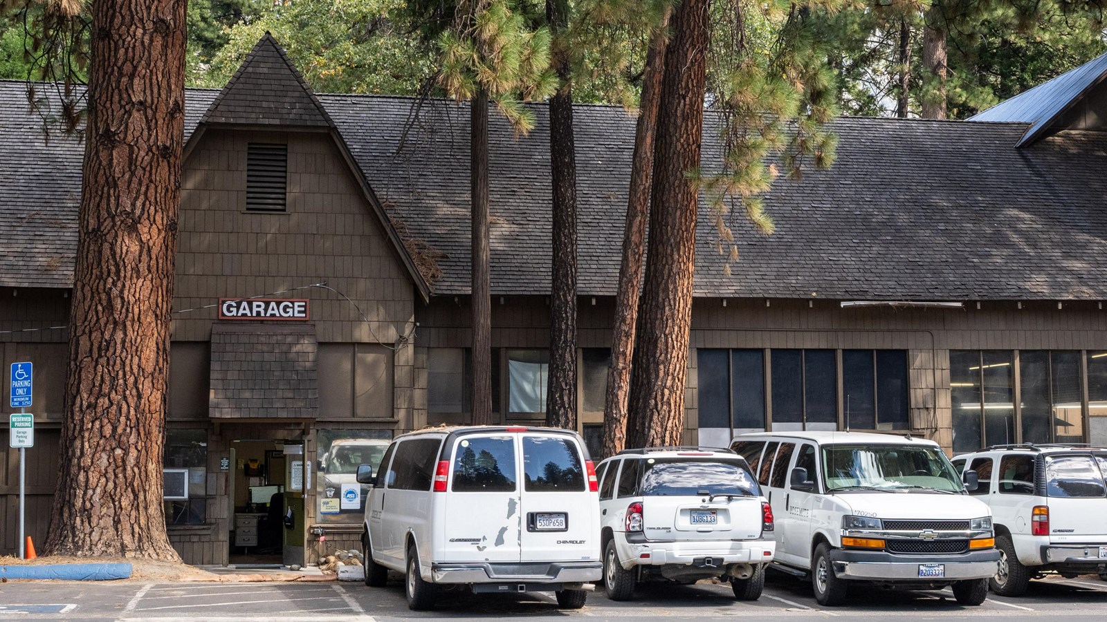 A brown building with a steep roof; white vehicles are parked in front of the building