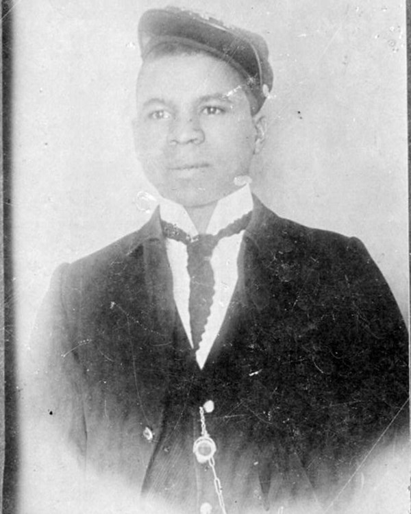 Black and white photo of African American man looking at the viewer. He has on a white shirt and tie