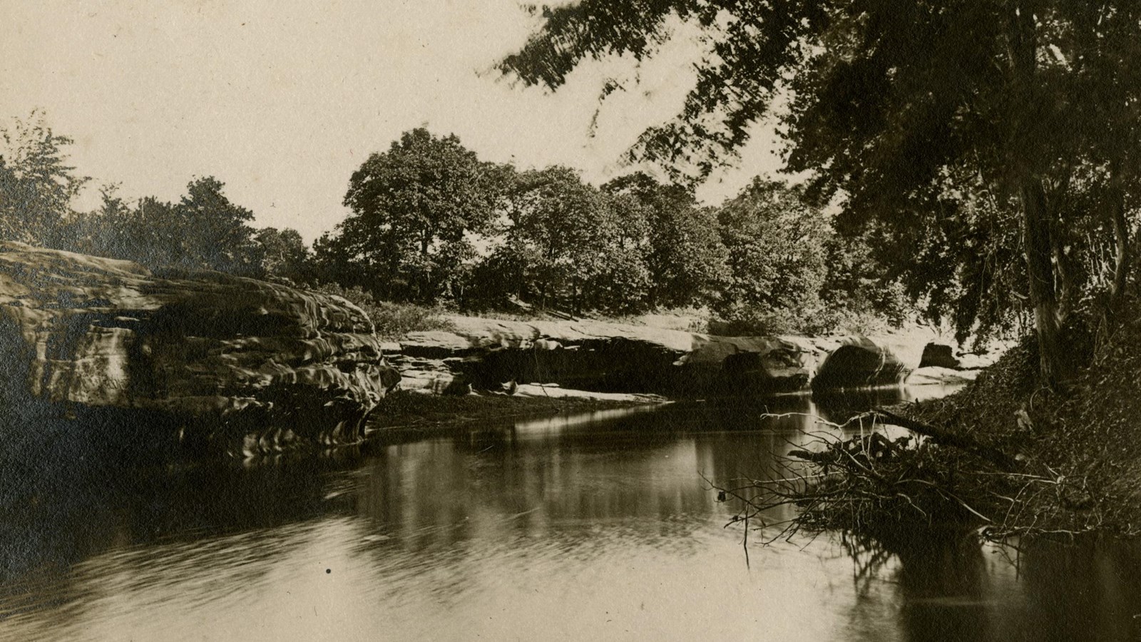 The Wakarusa River flows along a bend beneath limestone ledges. Trees grow thickly along the banks.