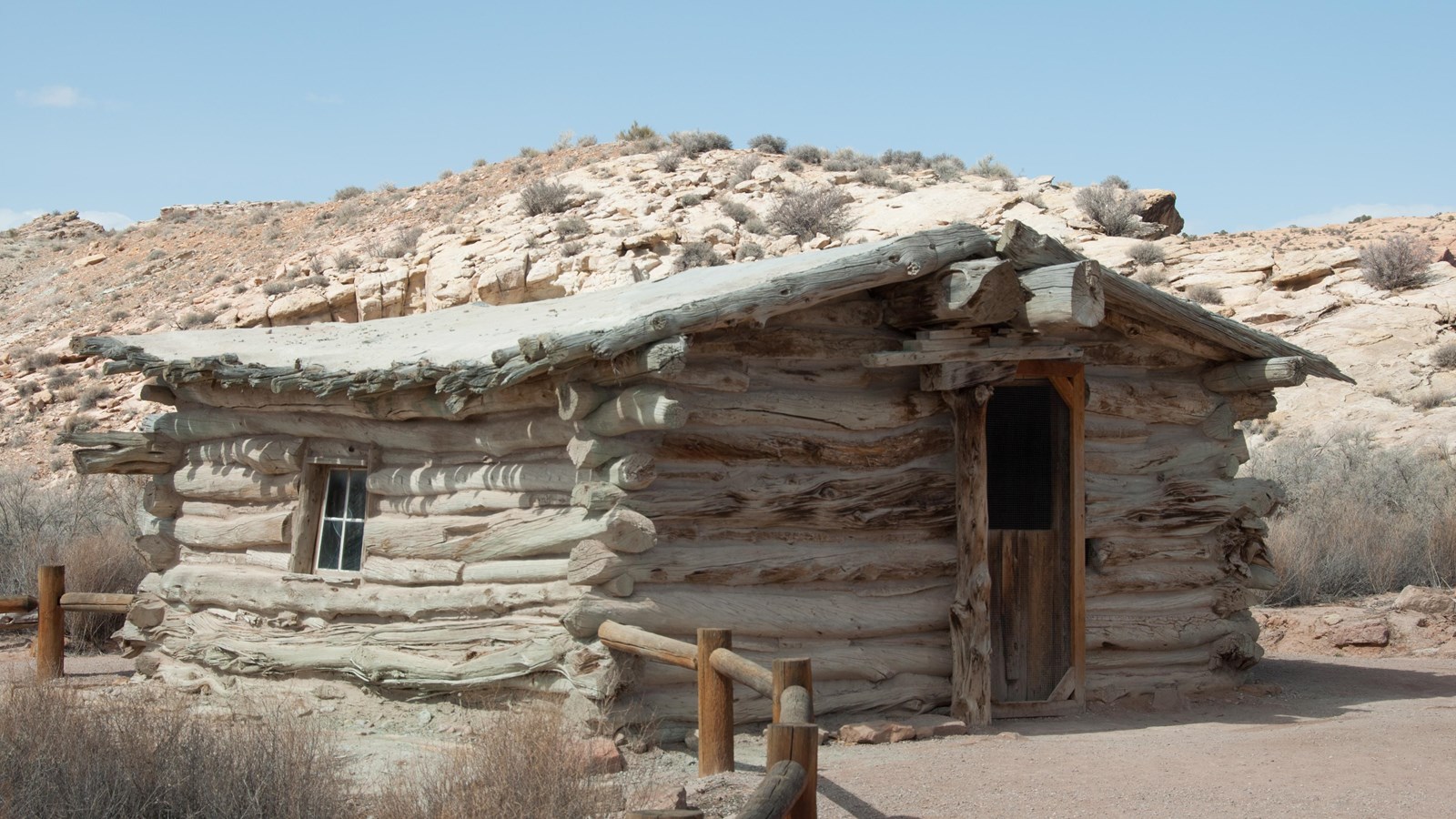 wooden cabin structure with a door surrounded by a wooden fence and shrubs