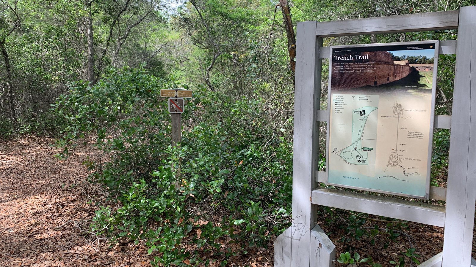 A trail sign stands next to a wooded path.