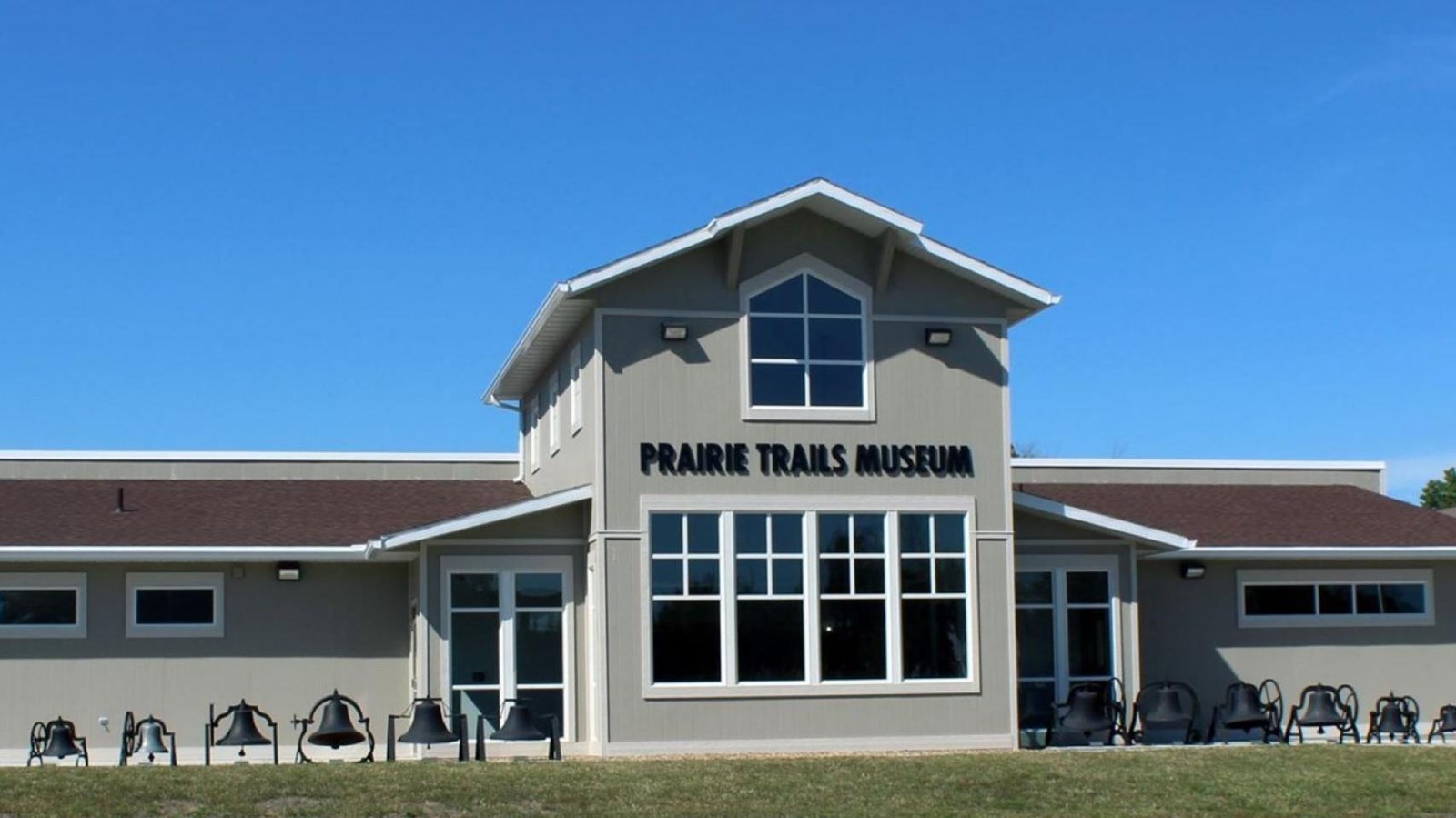 A gray building with a tall, windowed central section and horizontal wings on the left and right.