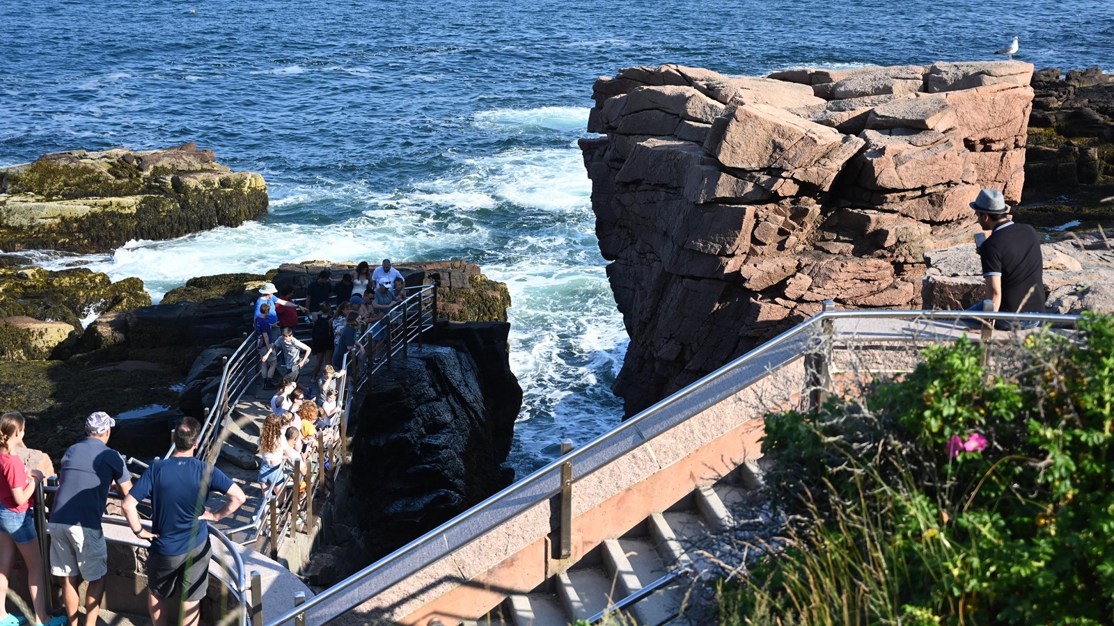 A large rock formation protrudes on the right side, with a set of stairs toward waters edge.