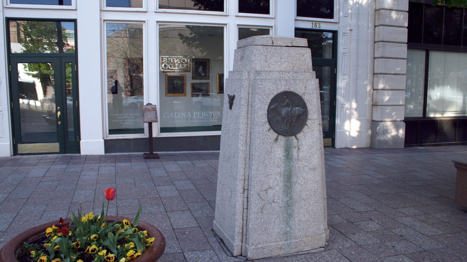 A stone monument sits in front of the entrance to a large building with large glass doors.