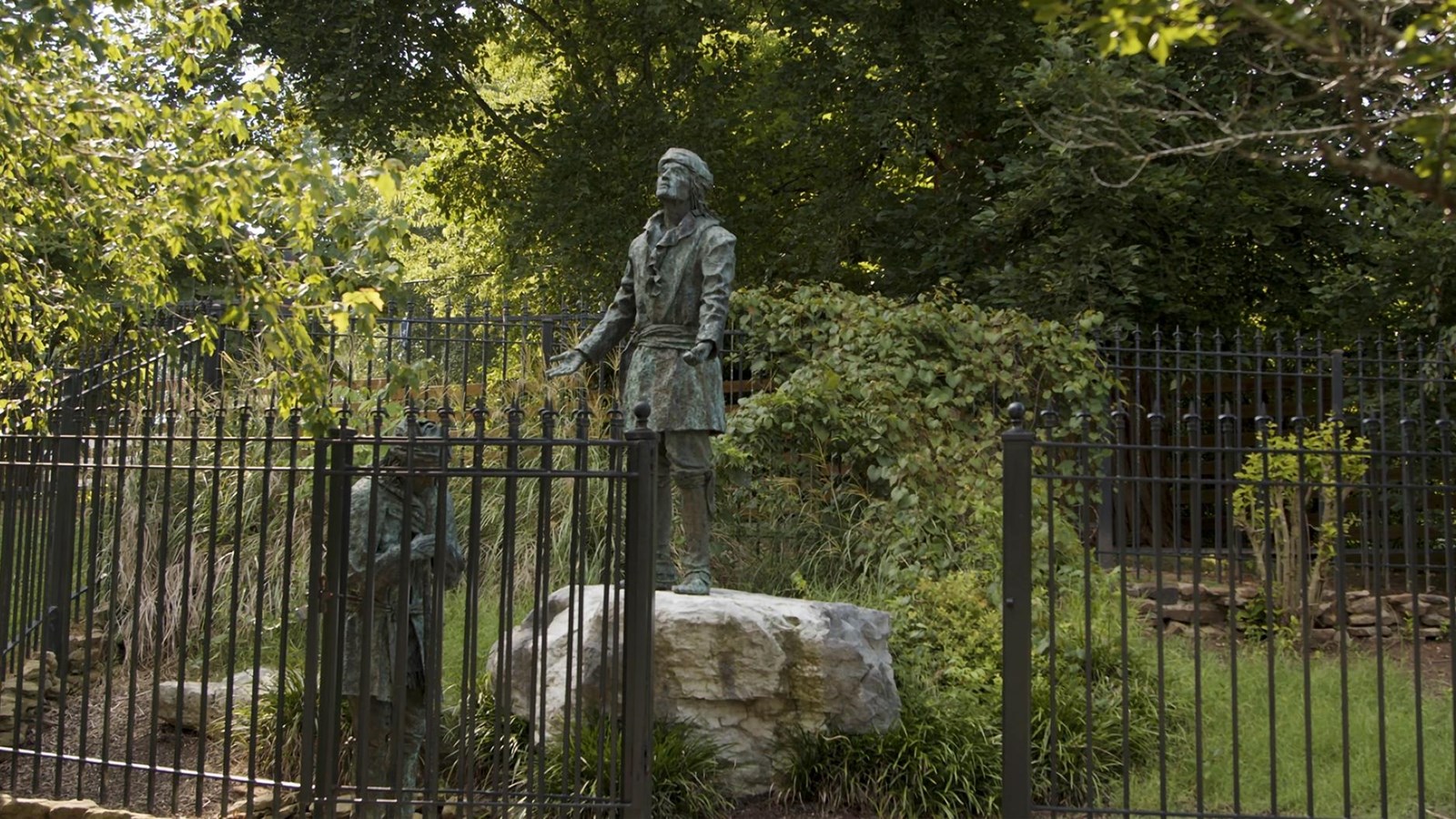 An iron gate surrounds two copper statues clothed in traditional Cherokee attire. 