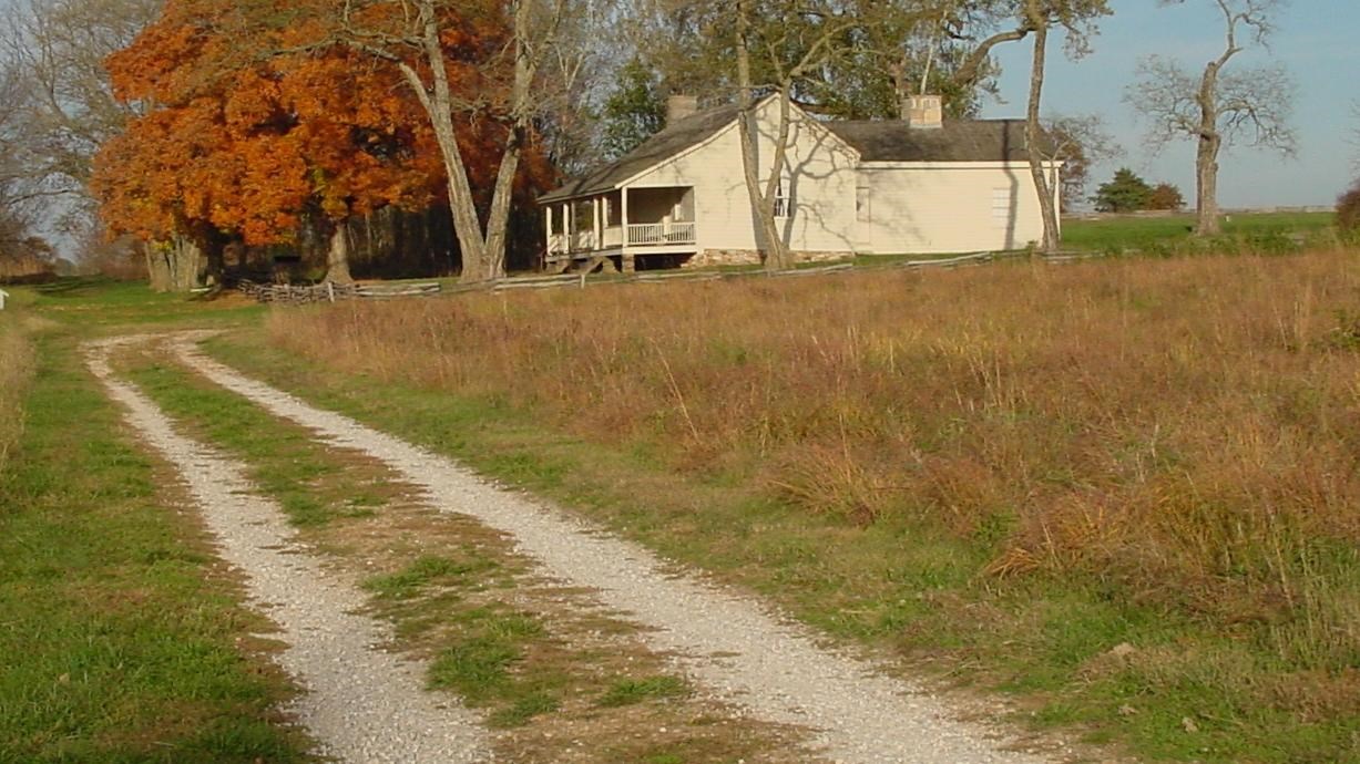 A two-lane unpaved road runs in front of a historic farm house