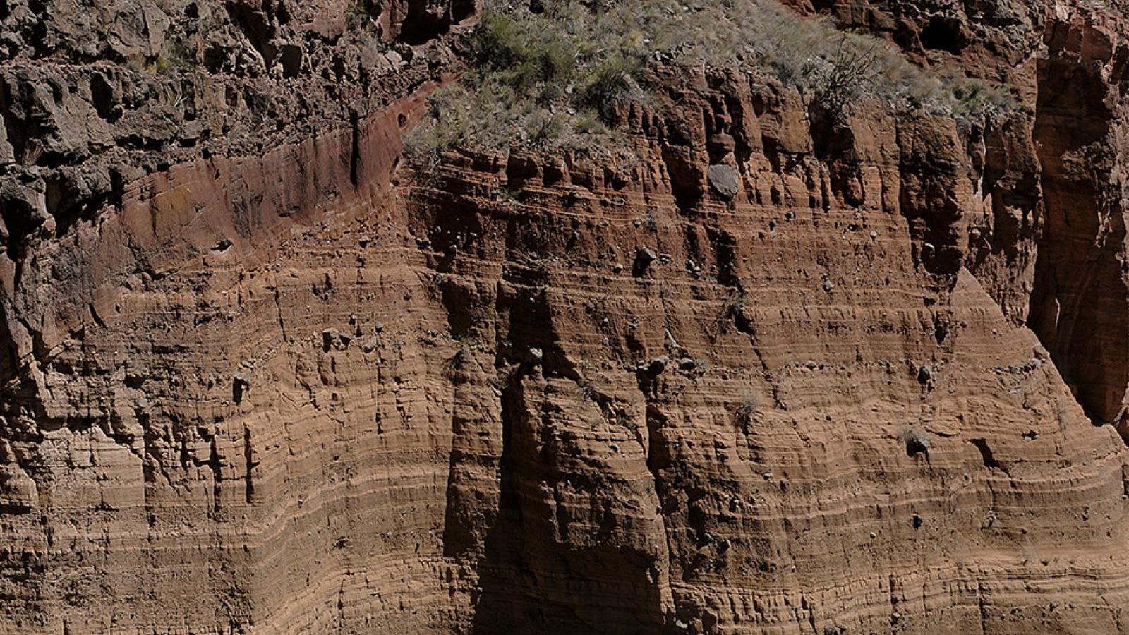 A sheer cliff face composed of many thin layers of different-colored deposits.