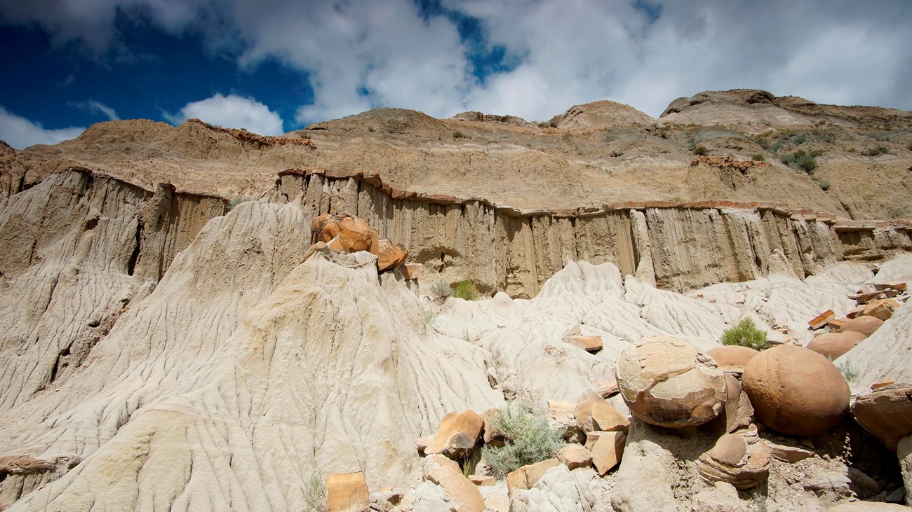 Several large round rocks eroded out of the side of a butte. The sky above the butte is cloudy blue.