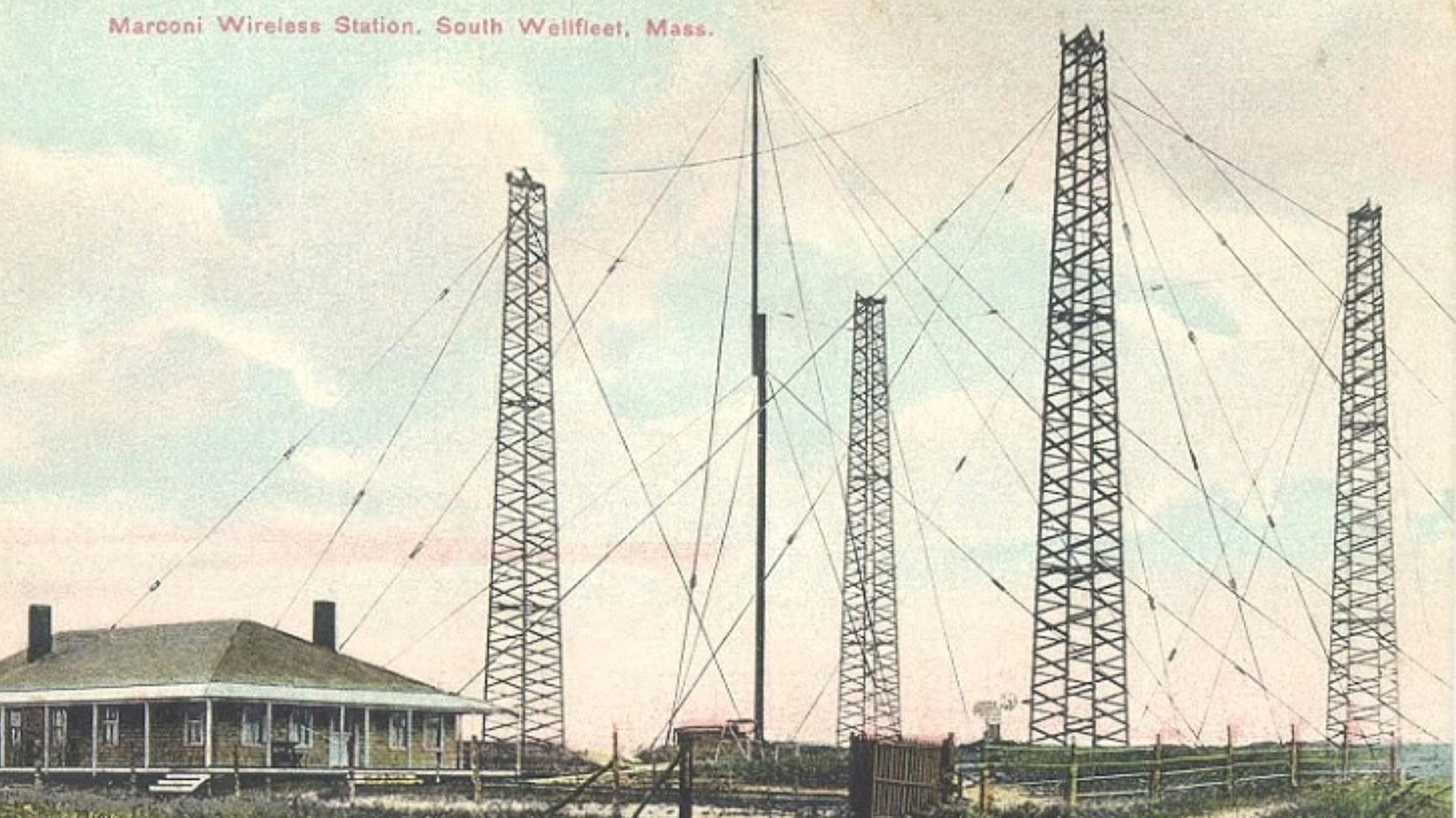 Postcard image of four large towers with wires connecting them. Office sits in the foreground.
