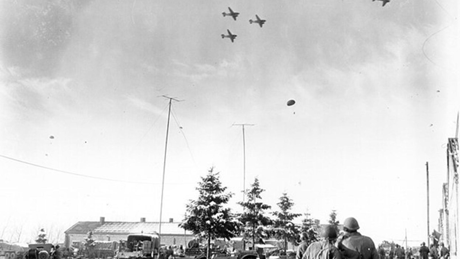 Uniformed men watch as supply boxes are dropped from the sky