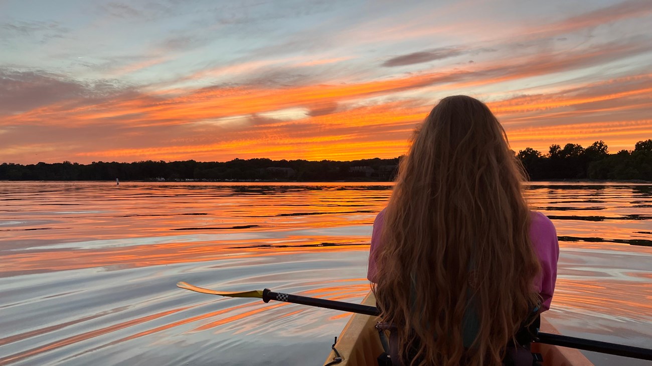 Person kayaking on a lake during a colorful sunset.