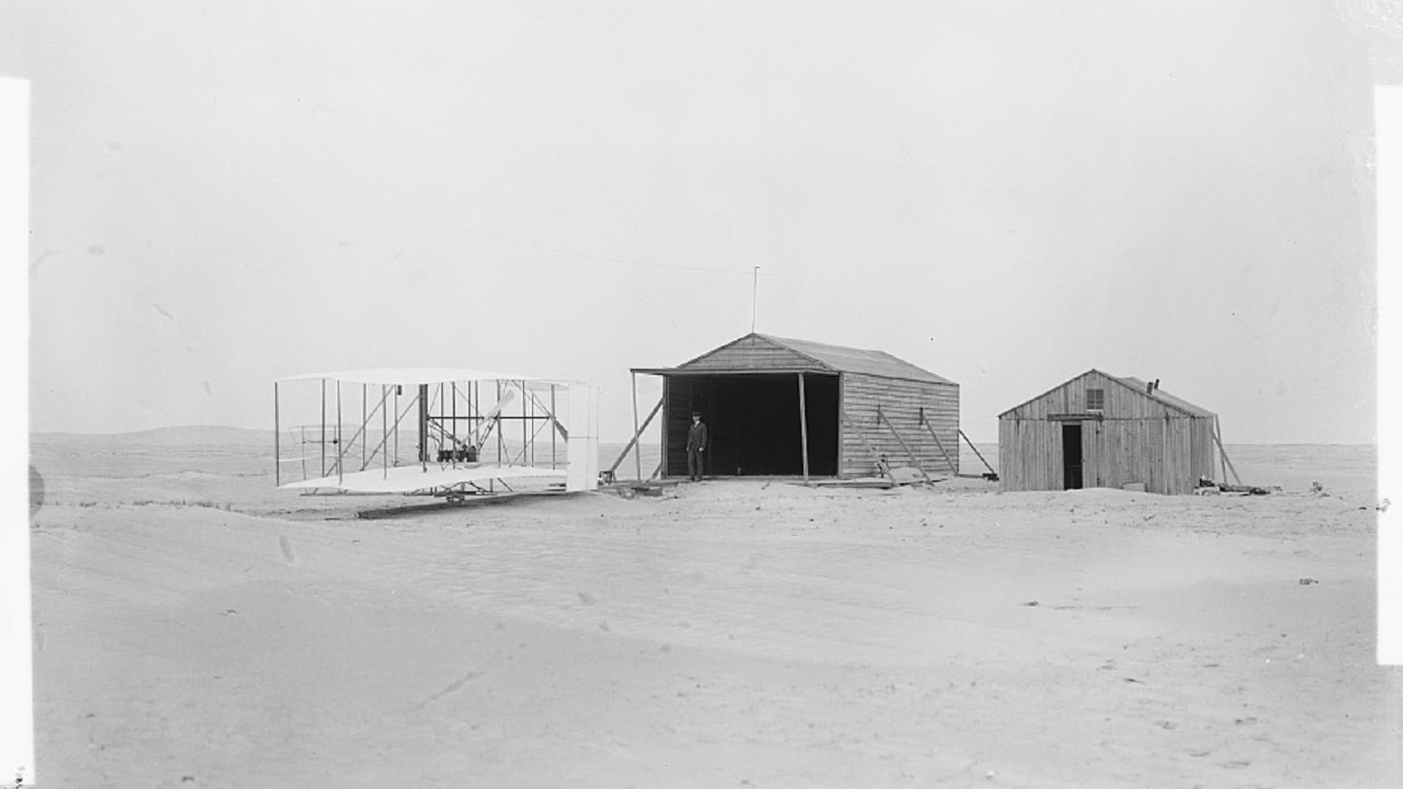 Black and white photograph of the 1903 flyer, the hangar and living quarters of the 1903 camp.