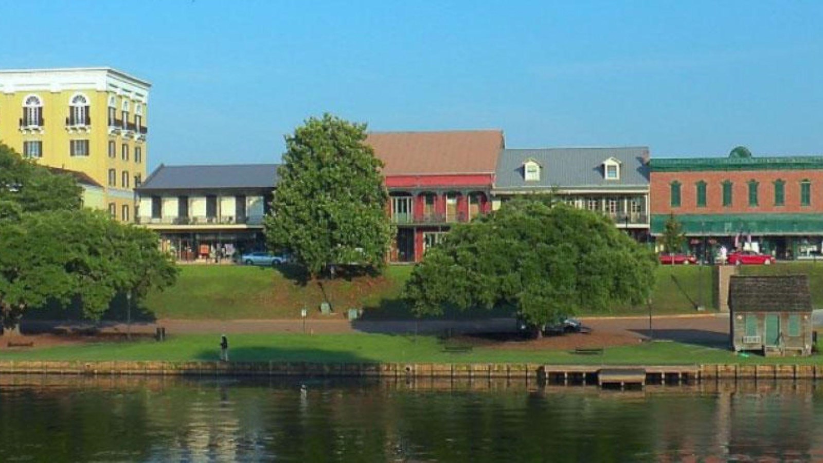 A river is lined with a tree filled park and historic buildings.
