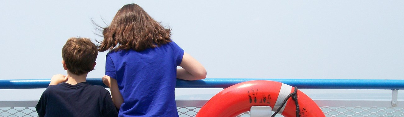 two youth looking at open water from deck of a large boat