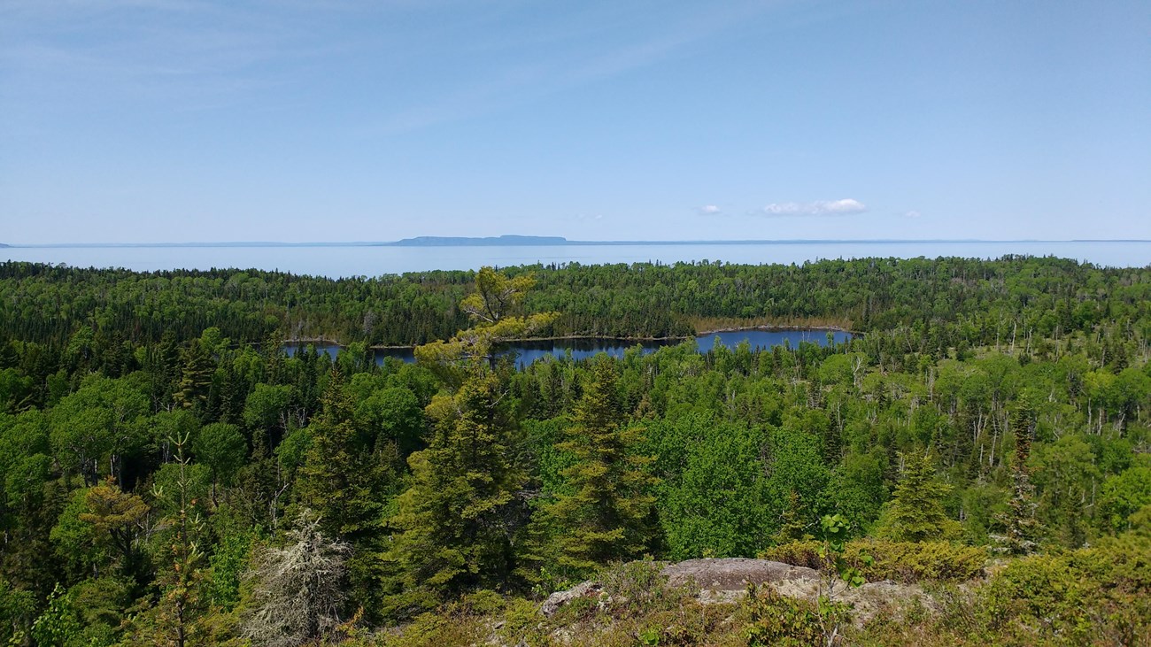 View from a ridge overlooking an interior lake, a forest, Lake Superior, and Canada\'s shoreline. 