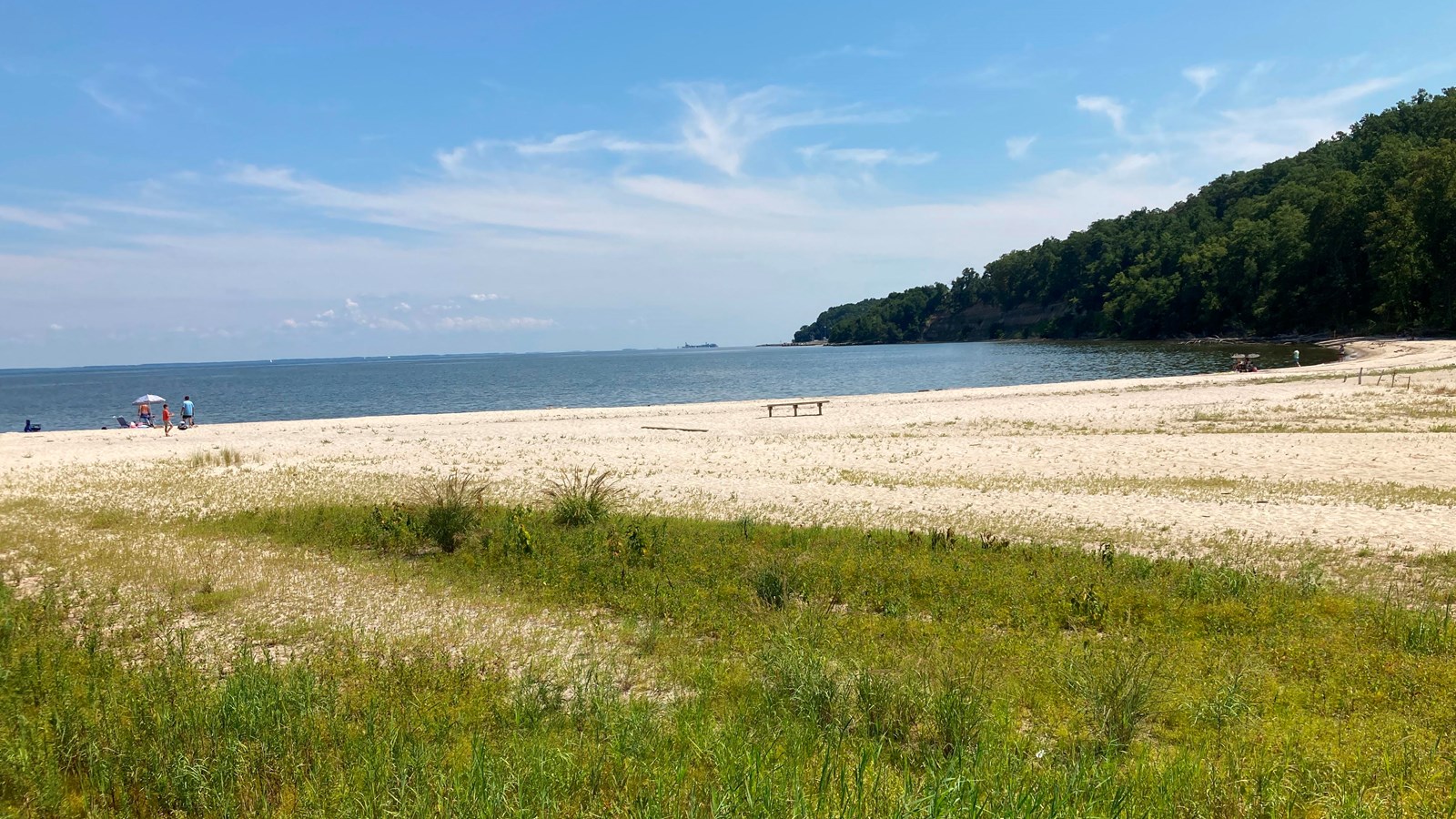 A few people stand on a sandy white beach.