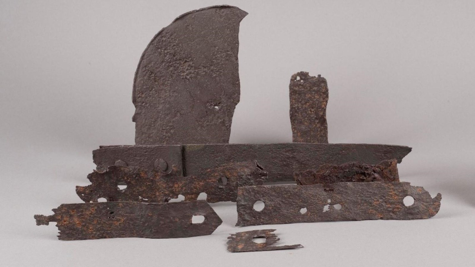 Strips of metal shaped with holes centered down the length. Ragged edges and some rust show aging